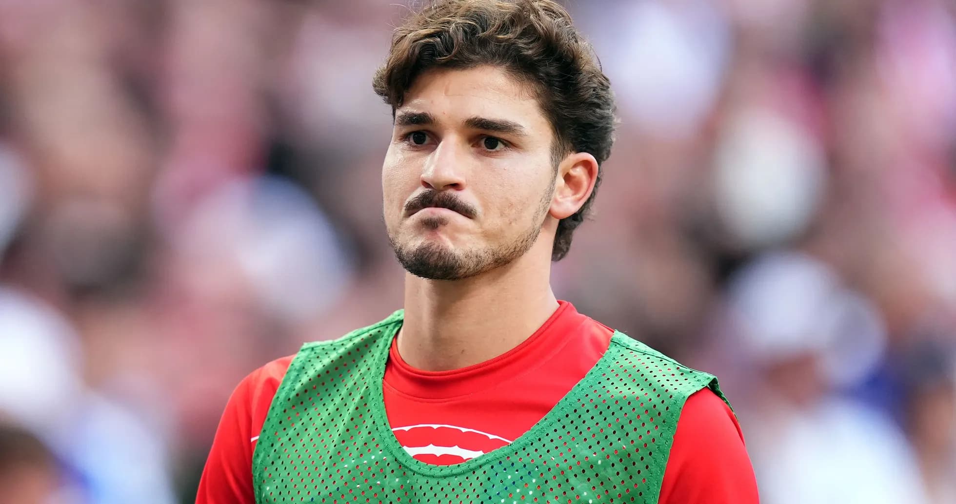 Joueur en attente sur le banc, maillot rouge et gilet vert