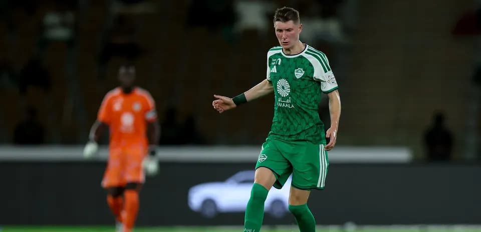 Joueur en maillot vert dribblant sur le terrain de football